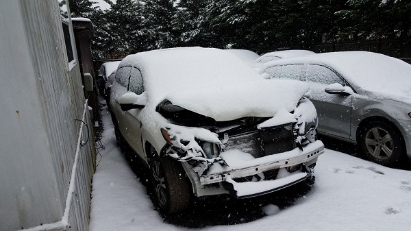 an SUV that has been heavily damaged in a car accident sites parked in the snow on a lot.