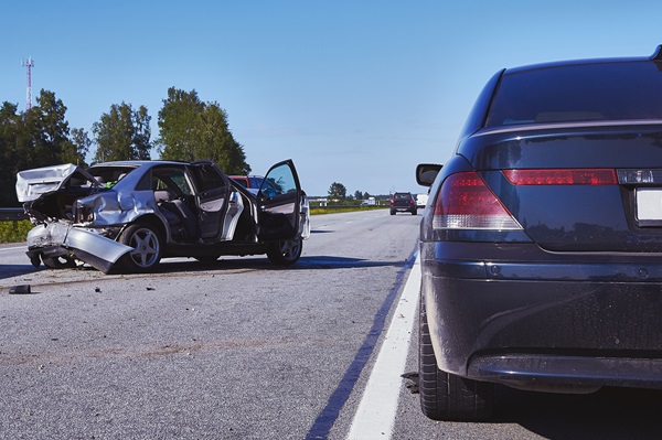 Two damaged cars sit on a highway after a serious collision, with debris scattered across the road.