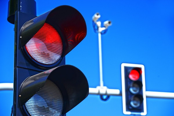 Close-up of red traffic lights with mounted cameras against a bright blue sky.