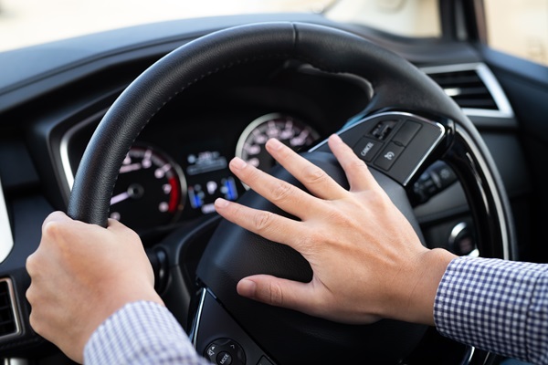 A pair of hands gripping a steering wheel and pressing the center horn pad forcefully, suggesting road rage.