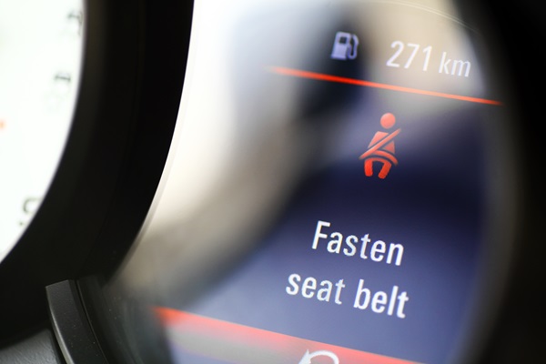 A car's digital dashboard display showing a red illuminated seat belt warning icon and the text "Fasten seat belt."